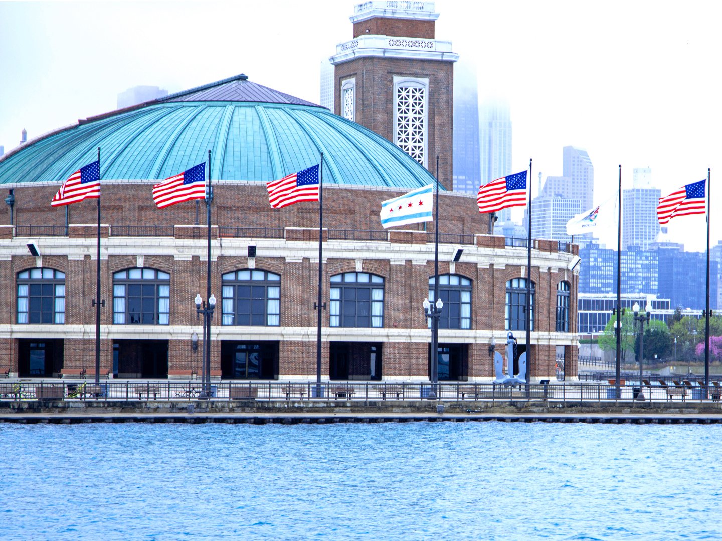 Exterior view of Navy Pier’s historic building lined with American flags, with the Chicago skyline and waterfront visible in the background.
