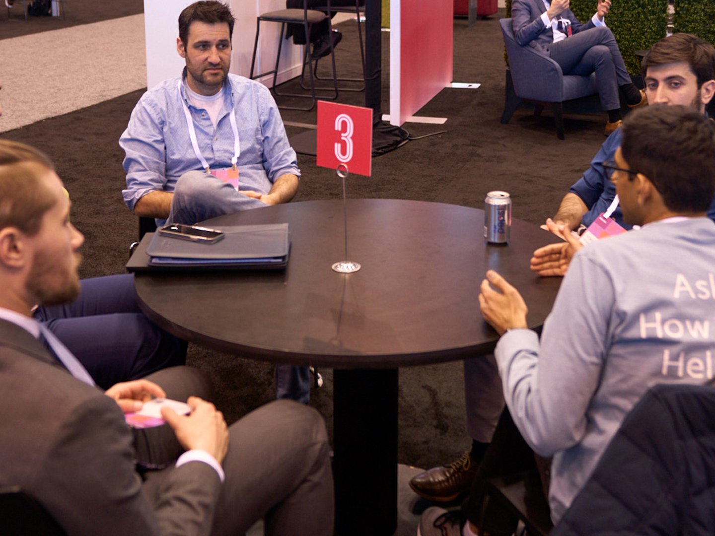 Several men discussing around a table with a large number 3 in the middle.