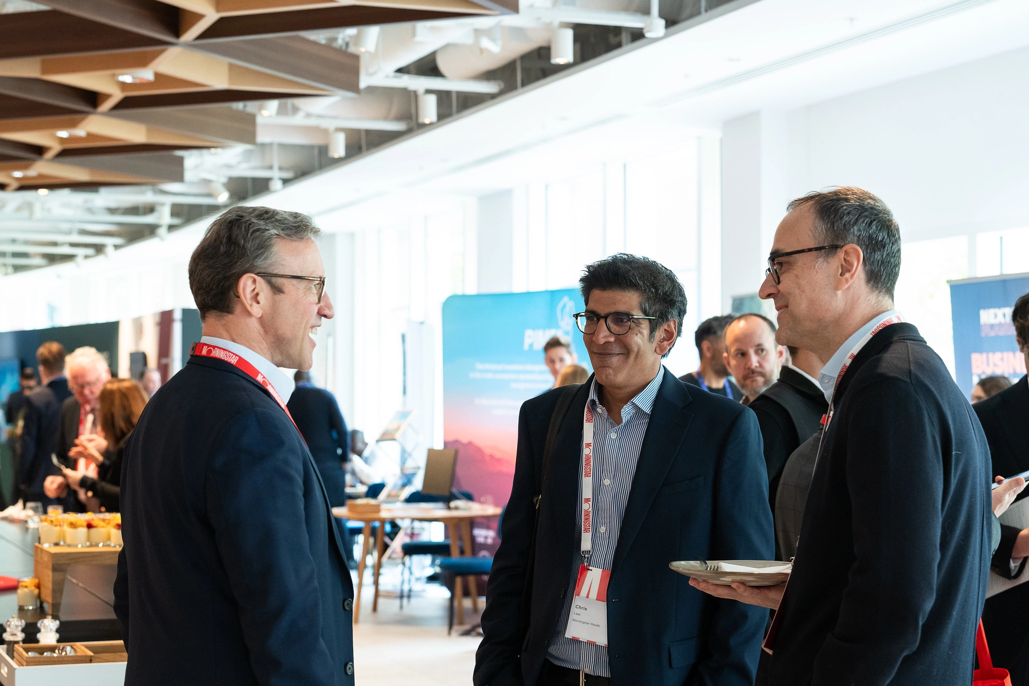 Three gentlemen talking in a circle. One person holding a plate with forks and knife. 
